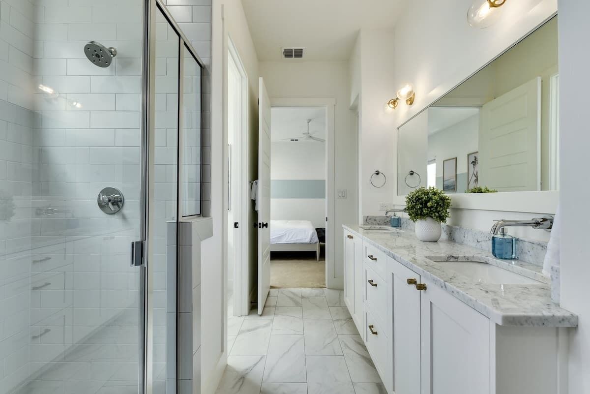 A modern bathroom with a glass shower enclosure, a large mirror, and a marble countertop.