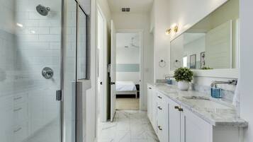 A modern bathroom with a glass shower enclosure, a large mirror, and a marble countertop.