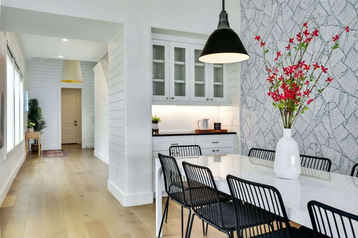 A modern kitchen with white cabinetry, a black pendant light, and a dining area with a white table and black chairs.