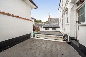 A narrow alleyway with a concrete floor, white walls, and a black baseboard. There are buildings on either side with visible windows and doors. - House - Sleeps 6 & paid off site parking available (Minehead)