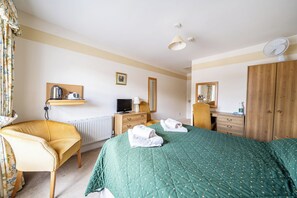 A hotel room with a bed, a chair, a desk, a television, a radiator, and a wardrobe. - House - Sleeps 6 & paid off site parking available (Minehead)