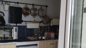 Cocina compacta con microondas, estufa y ollas colgantes. Hay una pizarra con un recordatorio de bebida y un refrigerador pequeño.