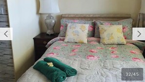 Un dormitorio con edredón estampado de flores, una mesita de noche con lámpara y una toalla verde sobre la cama.