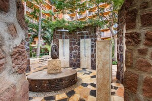 A stone-walled courtyard with a circular stone platform, a stone sculpture, and a metal shower enclosure.