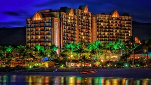 A multi-story hotel with balconies, a pool area, and palm trees.