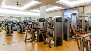 A gym with various exercise machines, a large screen, and a wooden floor.