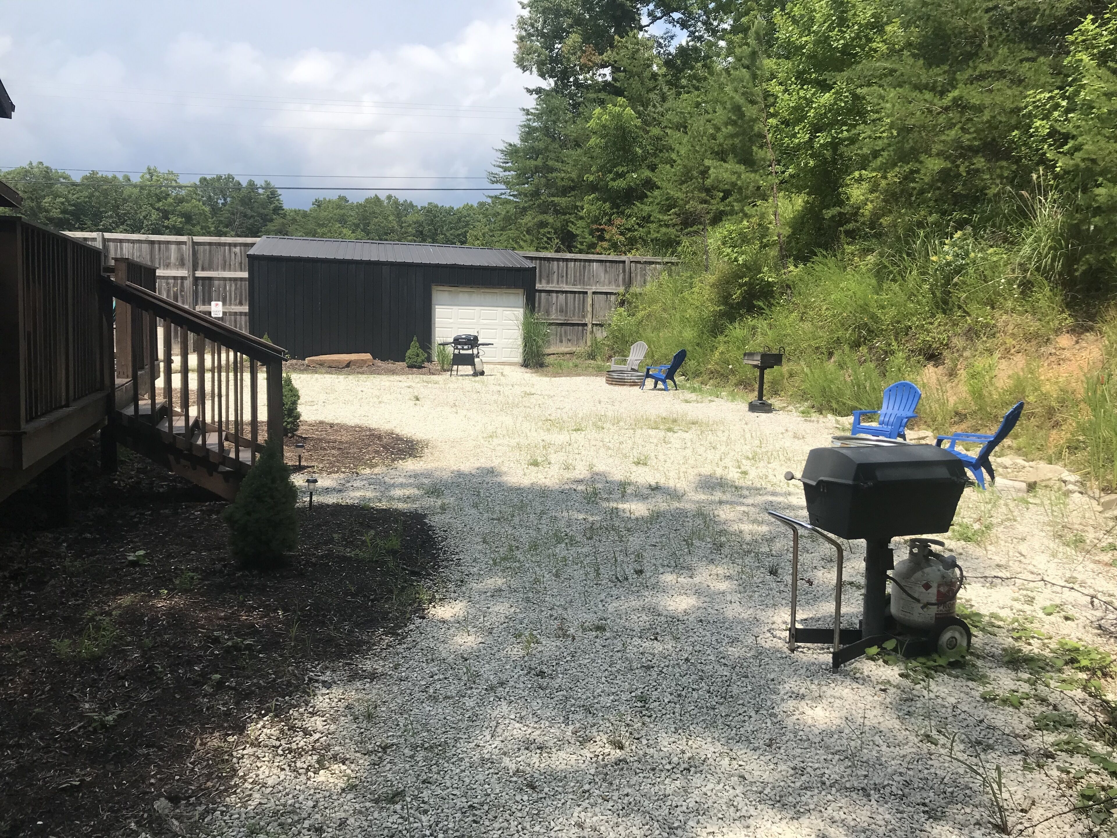 A backyard with a gravel path, a barbecue grill, and blue chairs.