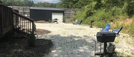 A backyard with a gravel path, a barbecue grill, and blue chairs.