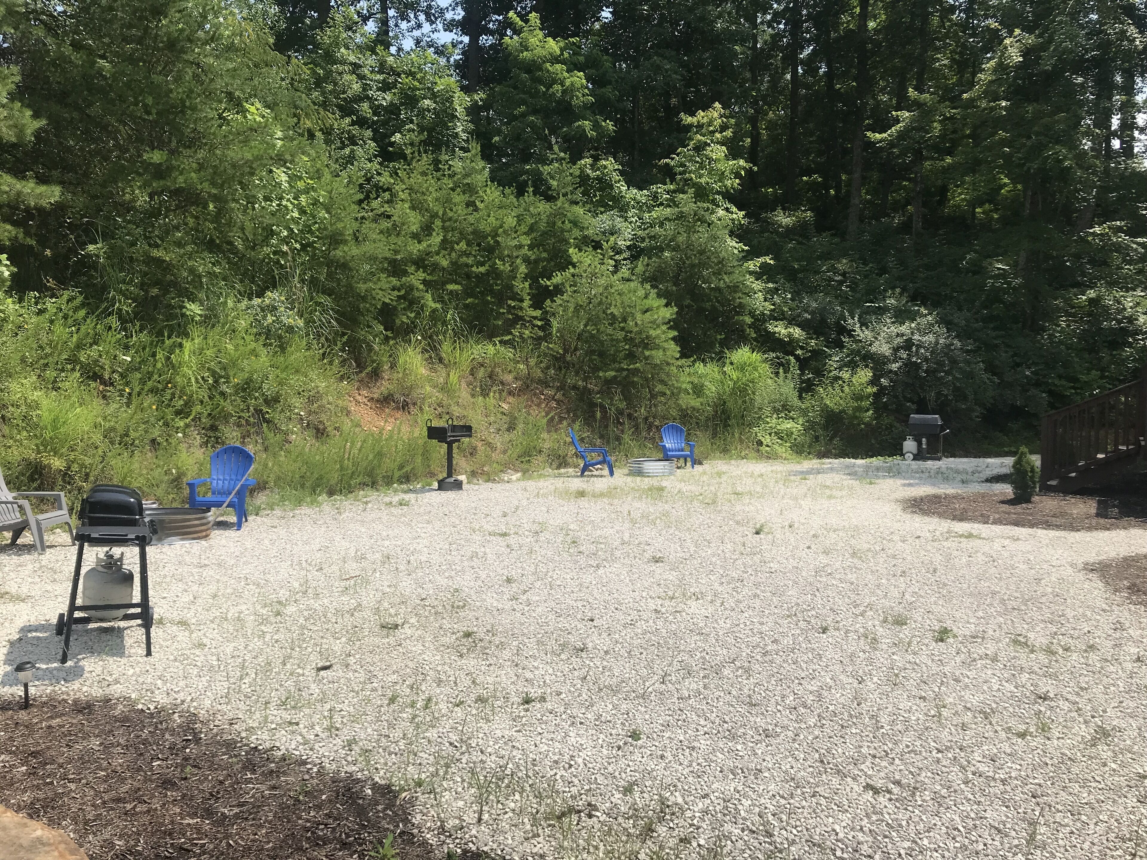 Un espace recouvert de gravier, avec plusieurs chaises Adirondack bleues, un barbecue et une boîte aux lettres.