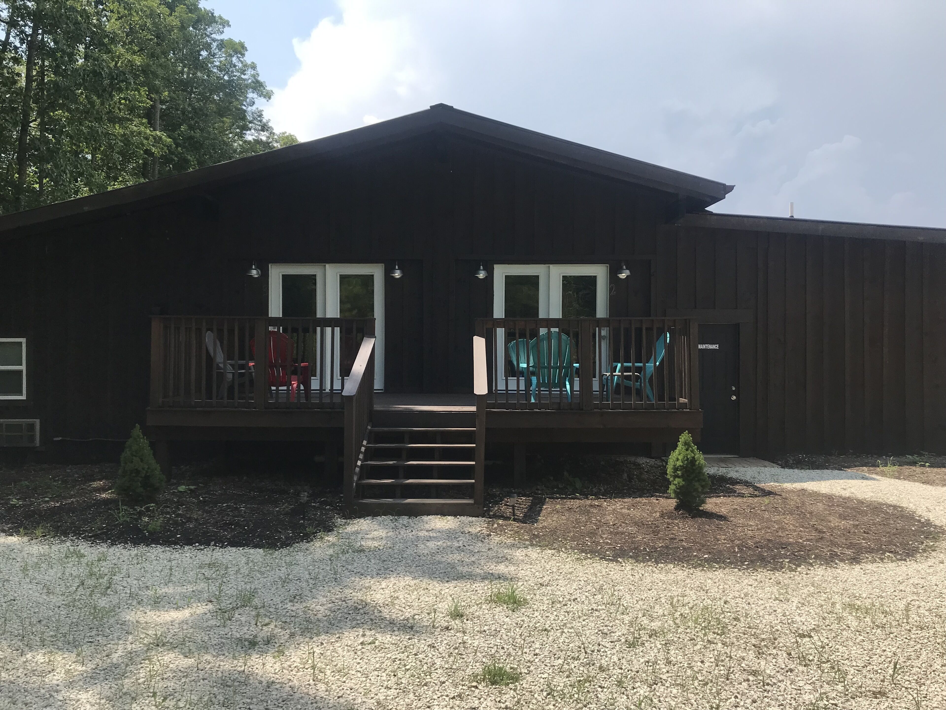 Une cabane à deux étages avec une terrasse en bois, deux portes d’entrée et un petit escalier menant à la terrasse.