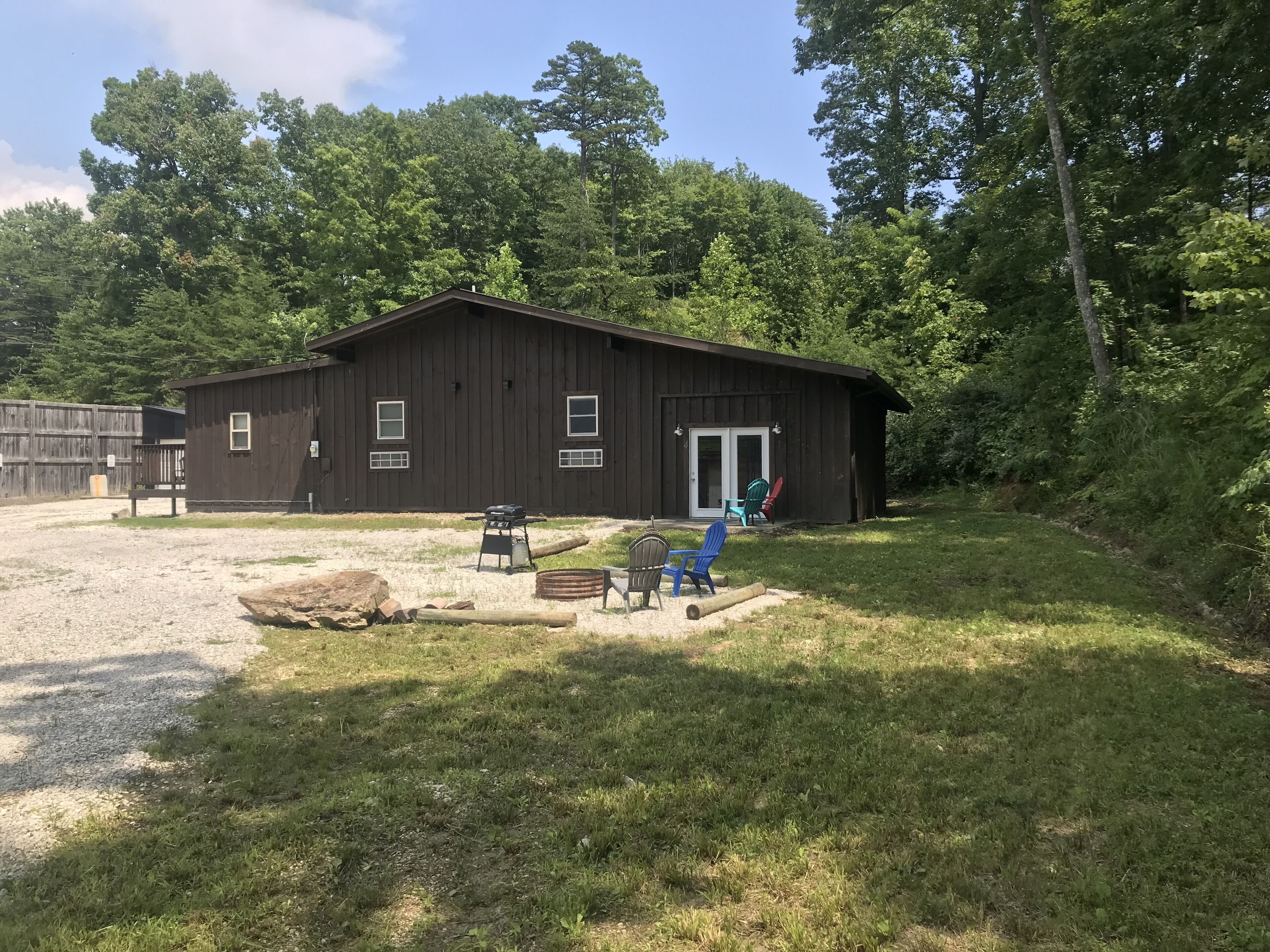 A rustic wooden building with a gravel driveway, a barbecue grill, and outdoor seating.
