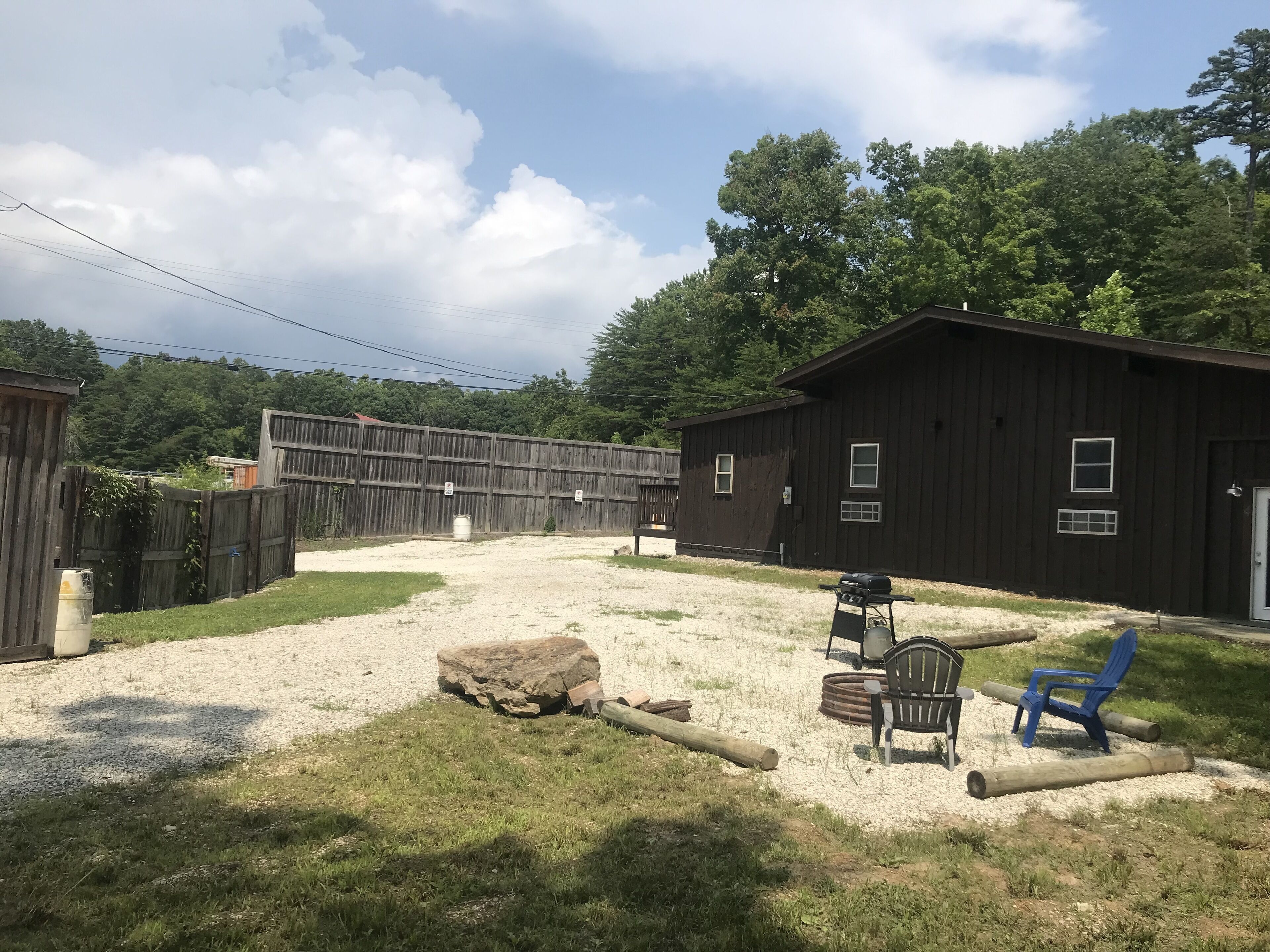 A rustic outdoor area with a gravel path, a wooden fence, a large rock, and a building with multiple windows.