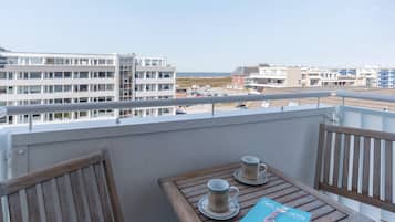 A balcony with a wooden table, two cups, and a book.