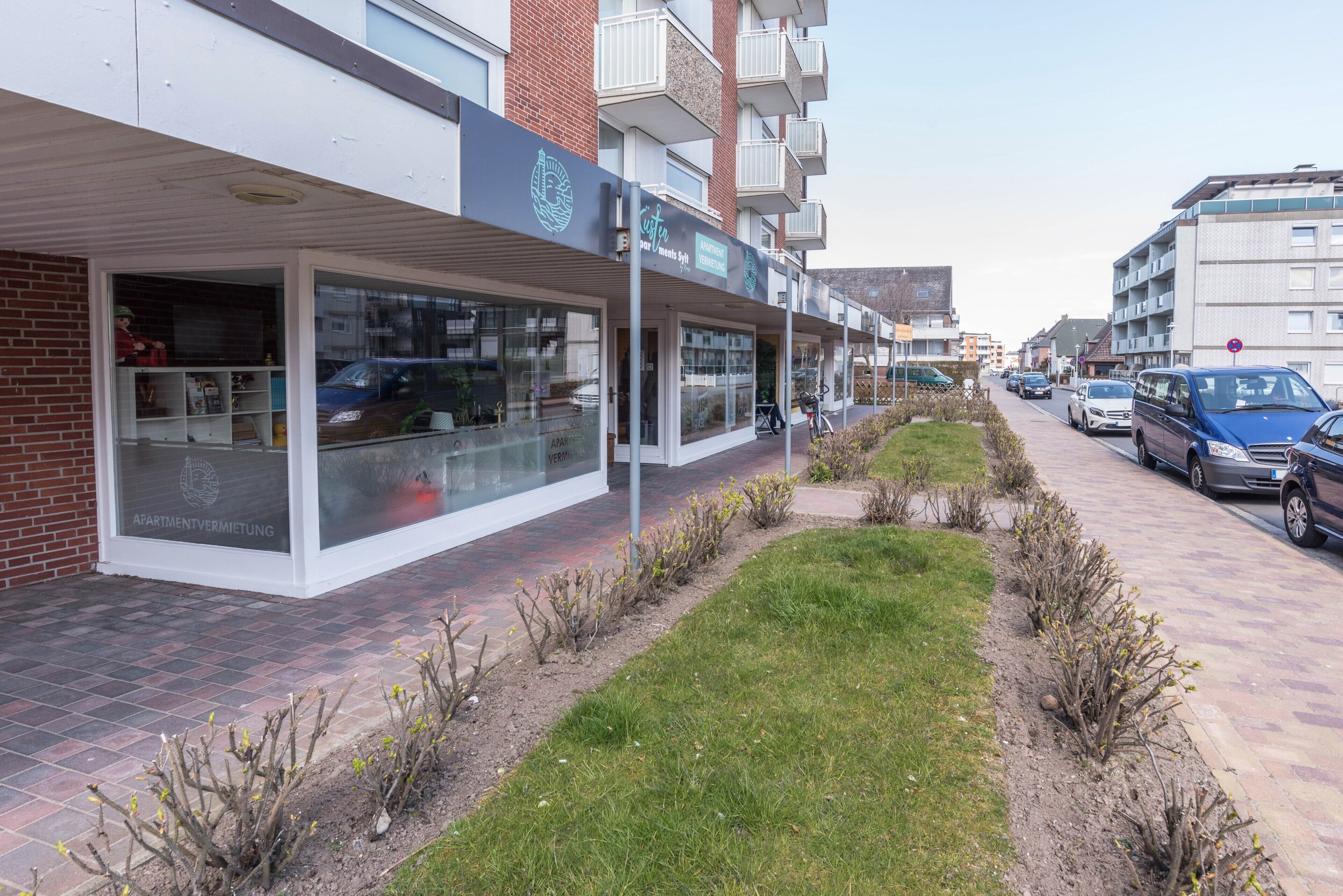 A modern building with a glass storefront, a brick facade, and a landscaped garden area.
