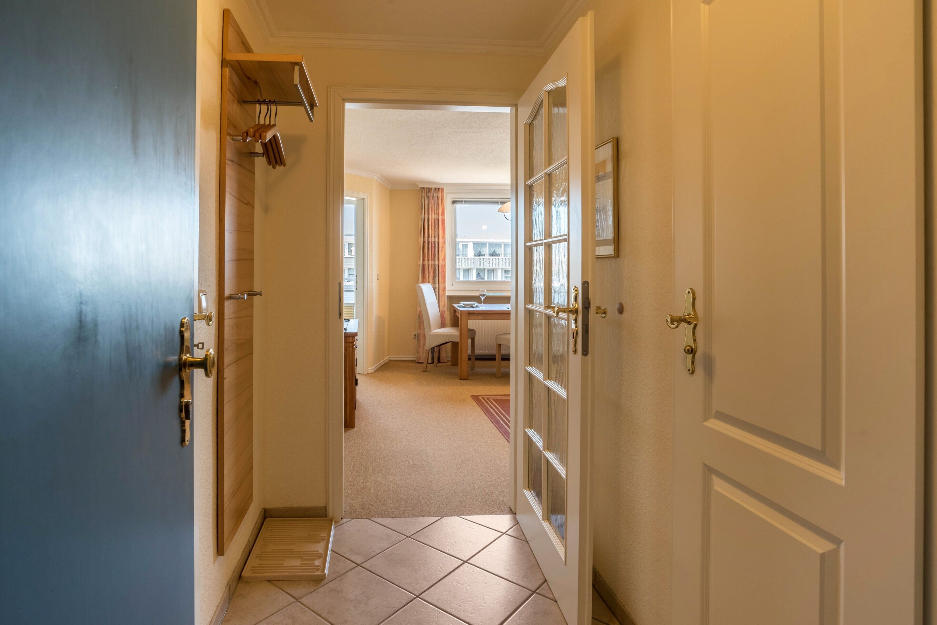 A hallway with a blue door, a white door with glass panels, and a view into a room with a chair and a table.