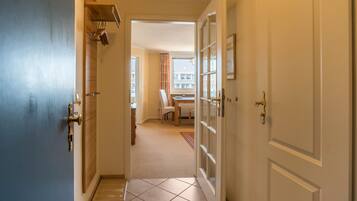 A hallway with a blue door, a white door with glass panels, and a view into a room with a chair and a table.