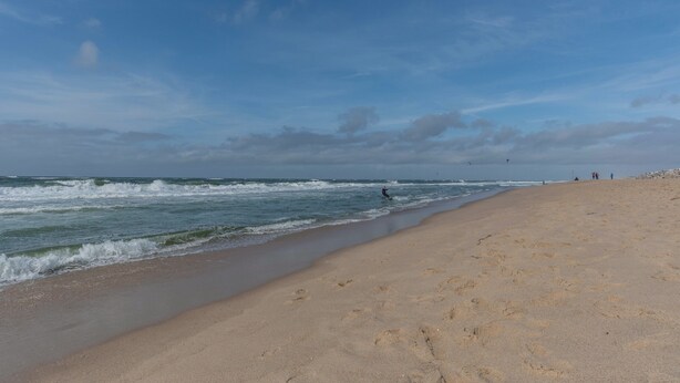 A beach with a sandy shore, ocean waves, and a person kite surfing.