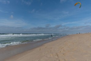 A beach with a sandy shore, ocean waves, and a person kite surfing.