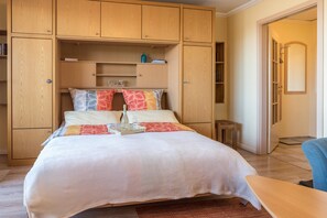 Un dormitorio con cama, armario de madera y una pequeña mesa.