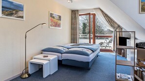 Ein Schlafzimmer mit einem Bett, Nachttischen, einer Stehlampe, einem Bücherregal und Blick ins Freie.
