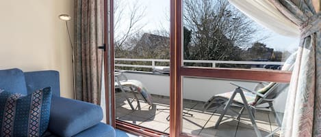 A room with a sofa, a sliding glass door leading to an outdoor area with a chair and a table.