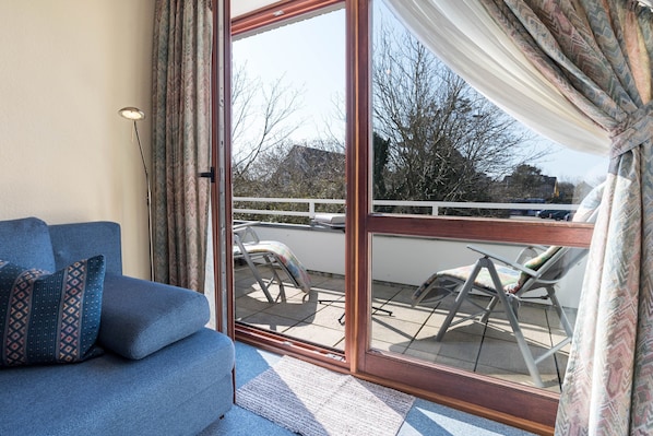 A room with a sofa, a sliding glass door leading to an outdoor area with a chair and a table.