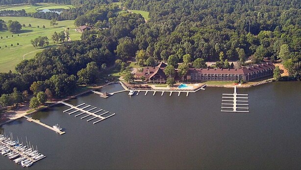 Vista aérea de una propiedad junto al lago con un muelle, una piscina y un edificio con techo rojo.