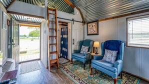 Una habitación acogedora con una escalera de madera, dos sillones azules, un tapete estampado y un ventilador de techo.