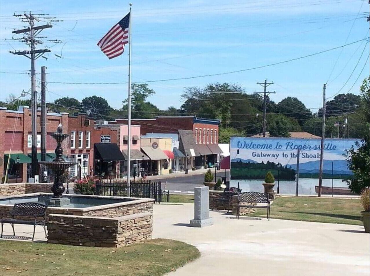 Una piazza cittadina con una fontana, panchine e una bandiera americana.