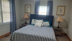 A neatly made bed with striped bedding, two bedside tables with lamps, and framed pictures on the walls. - Bella Vista - Waterfront Getaway, Kayaks, fishing & Close to Topsail Beaches! (Sneads Ferry)