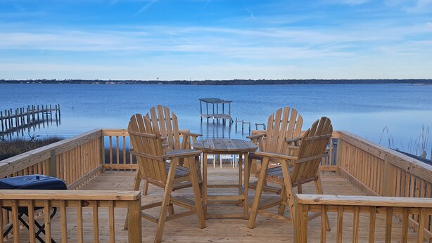 A wooden deck with chairs and a table overlooking a calm body of water. - Bella Vista - Waterfront Getaway, Kayaks, fishing & Close to Topsail Beaches! (Sneads Ferry)