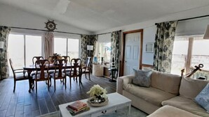A spacious living room with a dining area, a sofa, and a coffee table. - Bella Vista - Waterfront Getaway, Kayaks, fishing & Close to Topsail Beaches! (Sneads Ferry)