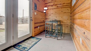 A wooden cabin interior with a door leading outside, a metal table, and a light fixture. - Cabin in RRG• Pet Friendly • Hi Speed 🛜 Hikers Welcome (Pine Ridge)