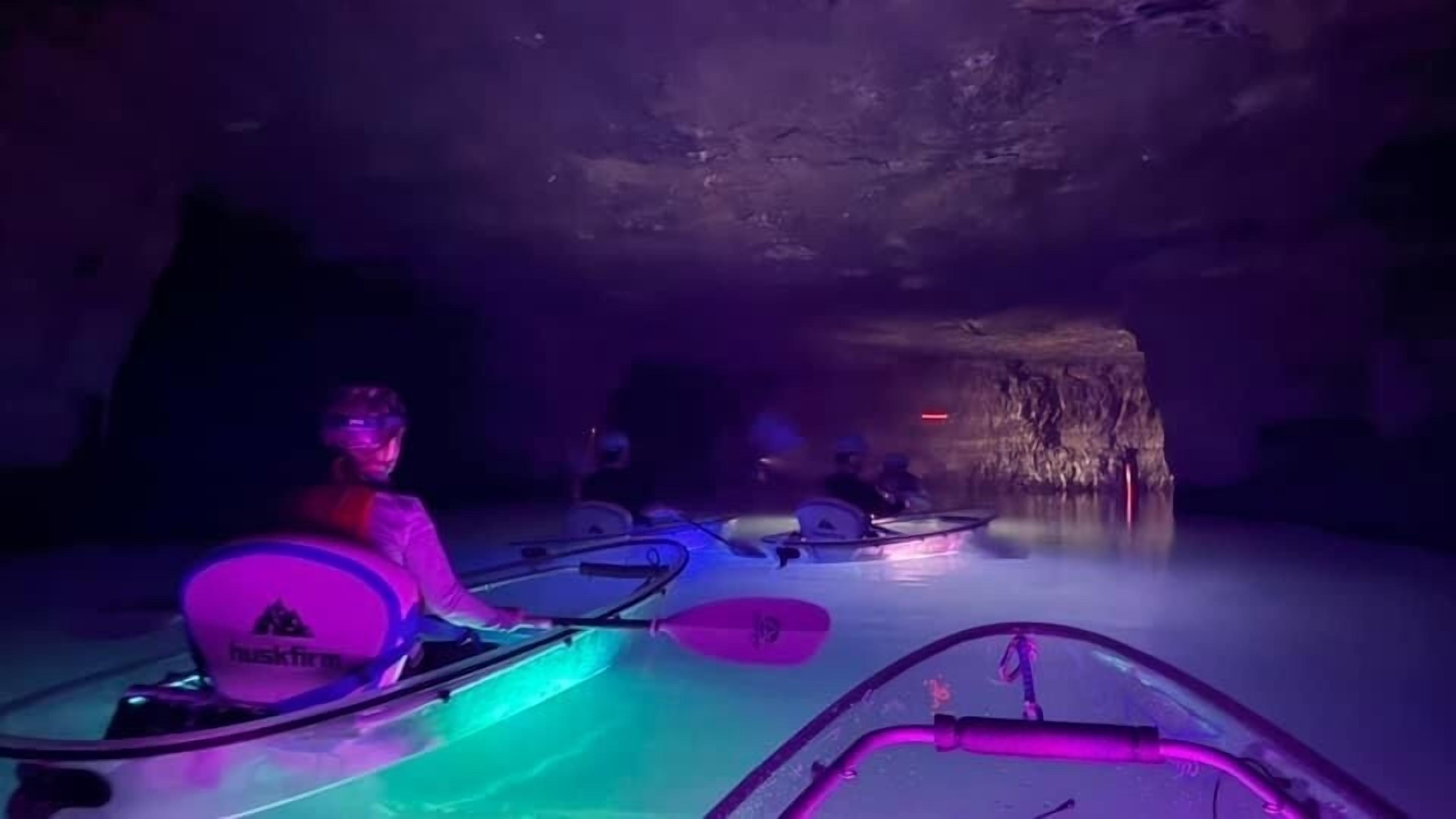 A group of people kayaking in a dimly lit cave with colorful lighting.