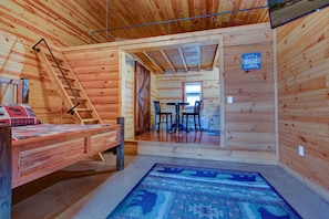 Cozy cabin-style room with a bed, wooden ladder, and small table with two chairs.