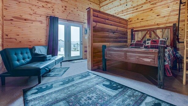 A cozy cabin interior with a sofa, a bed with plaid bedding, and a wooden ceiling. - Cabin in RRG• Pet Friendly • Hi Speed 🛜 Hikers Welcome (Pine Ridge)