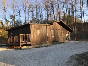 A wooden cabin with a porch, a gravel driveway, and a forested background. - Cabin in RRG• Pet Friendly • Hi Speed 🛜 Hikers Welcome (Pine Ridge)
