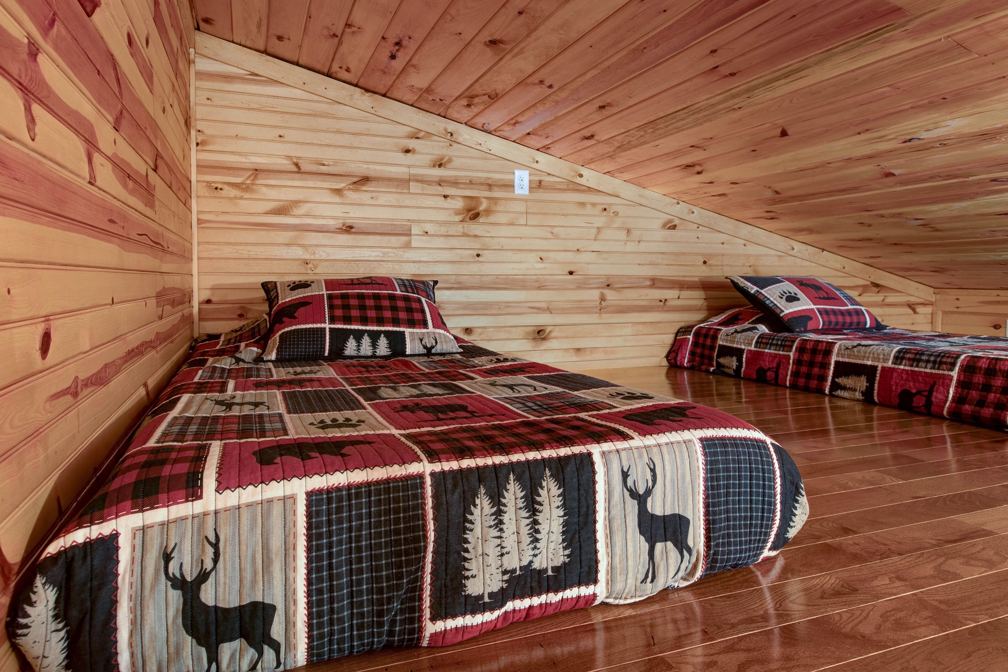 A cabin with two beds, each with a red and black checkered quilt featuring forest and deer patterns.