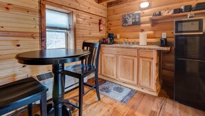 A wooden cabin interior with a dining table, chairs, a kitchen area including a refrigerator, microwave, and coffee maker. - Cabin in RRG• Pet Friendly • Hi Speed 🛜 Hikers Welcome (Pine Ridge)