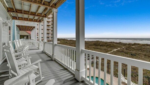 Eine überdachte Veranda mit weißen Geländern und Blick auf den Strand.