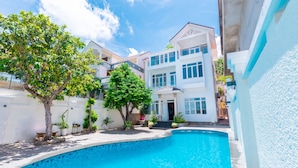 A residential property with a swimming pool, a two-story house, and a garden with trees and plants.