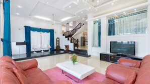 A spacious living room with a large TV, leather sofas, a white coffee table, and a staircase leading to an upper level.