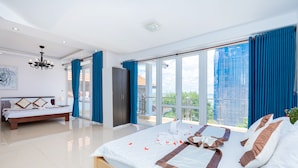 A spacious bedroom with a large bed, a separate sofa bed, and a balcony with a view of the city.