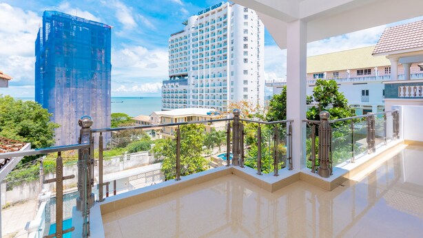 A hotel balcony with a view of a tall building, pool, and greenery.