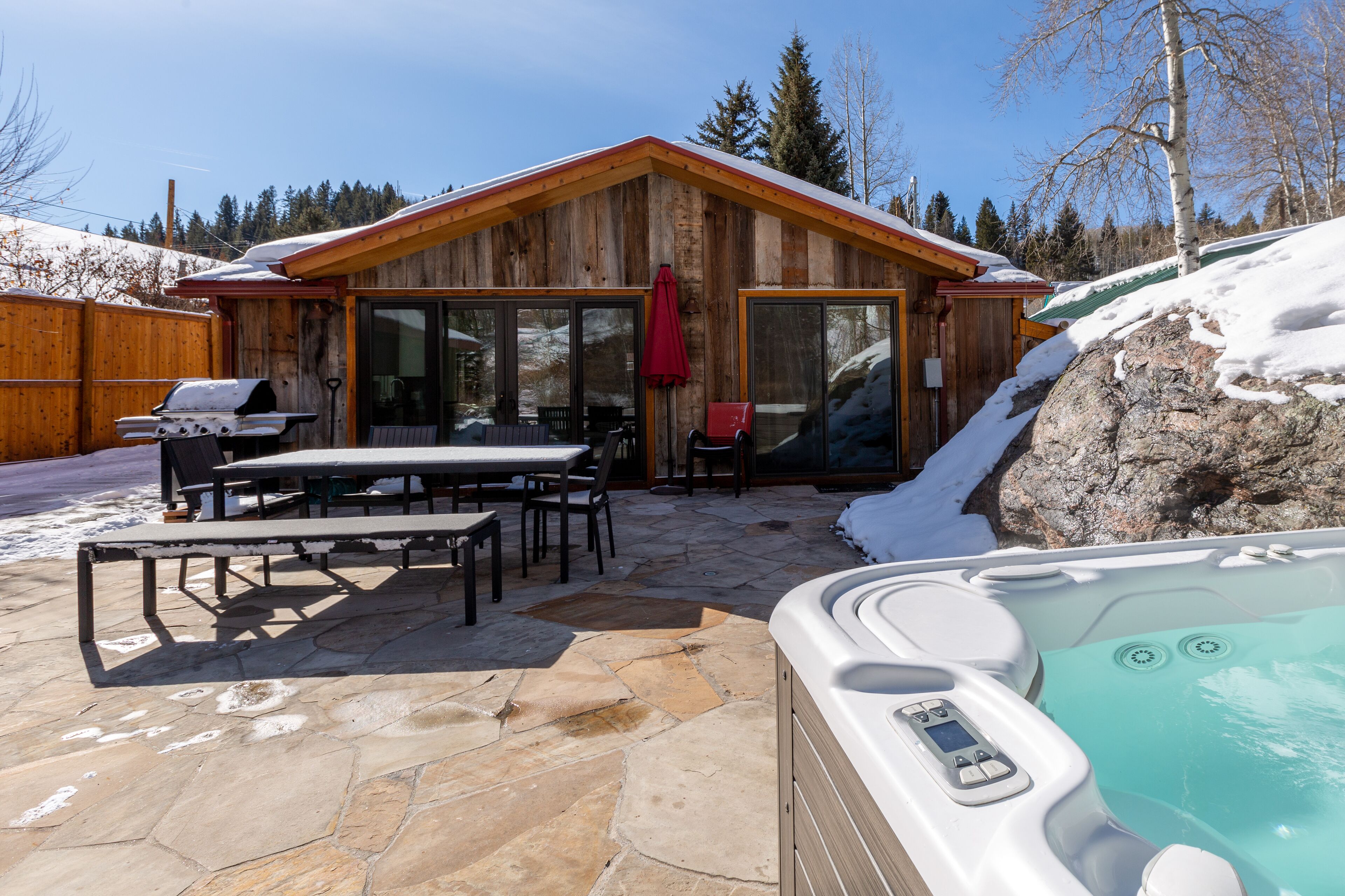 A wooden cabin with a hot tub, stone patio, and a barbecue grill.