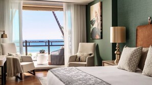 Une chambre d’hôtel avec un grand lit, deux fauteuils, une table d’appoint et une vue sur l’océan.