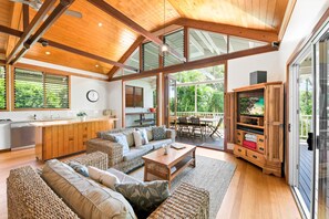 A spacious living area with a wooden ceiling, large windows, a kitchen, and a TV entertainment unit. - Serenity - Eco friendly, pet friendly beach house with pool (Sunshine Coast)