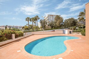 Une piscine à bord incurvé, entourée d’une terrasse carrelée.