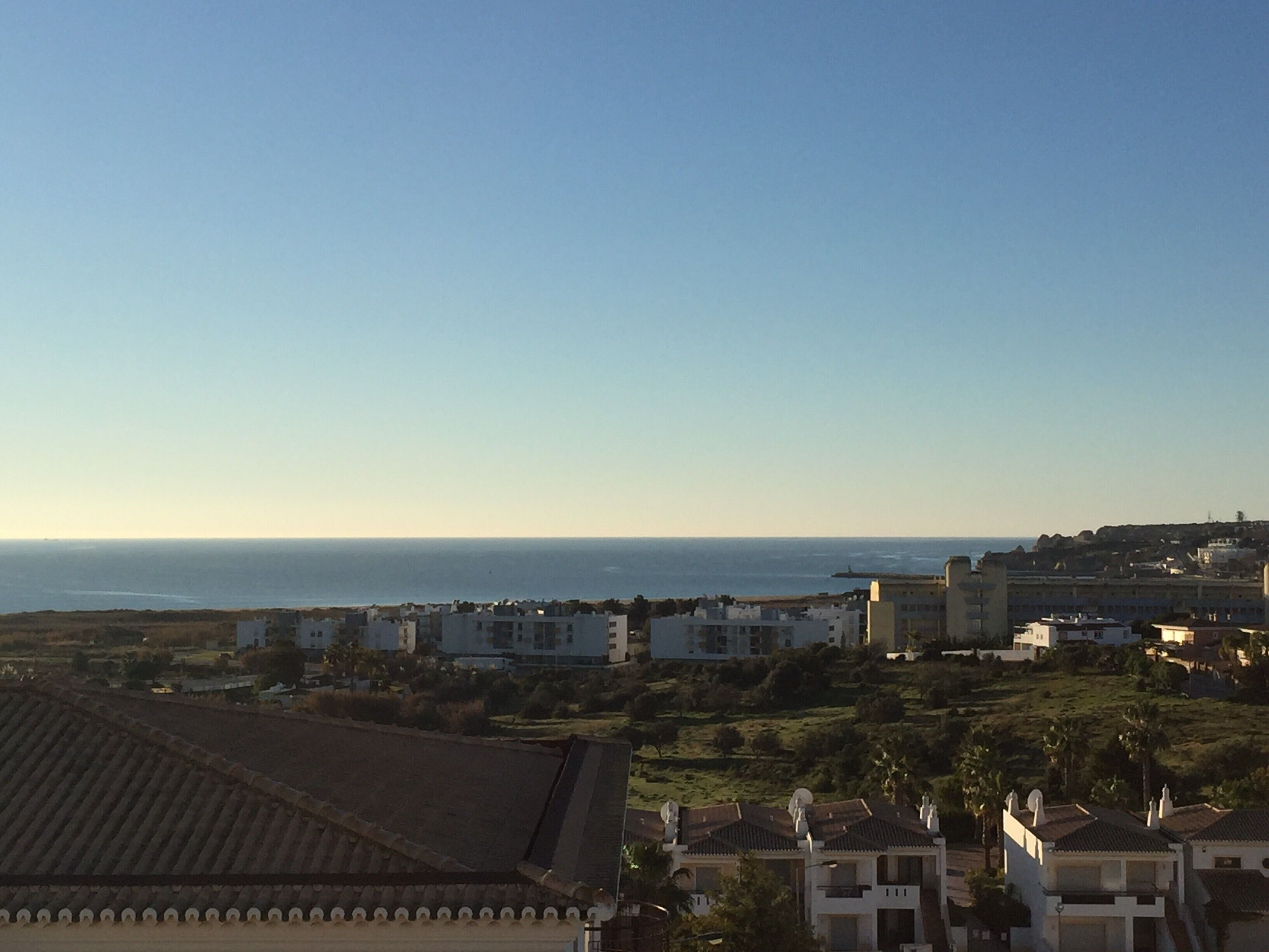 Eine Küstenstadtlandschaft mit Gebäuden, einem klaren Himmel und dem Meer im Hintergrund.