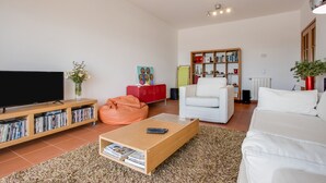 A living room with a flat-screen TV, a bookshelf, a white sofa, a coffee table, and a bean bag. - Apartment "Meia Praia Beach" with Sea View, Pool, Wi-Fi, Balcony & Garden (Lagos)